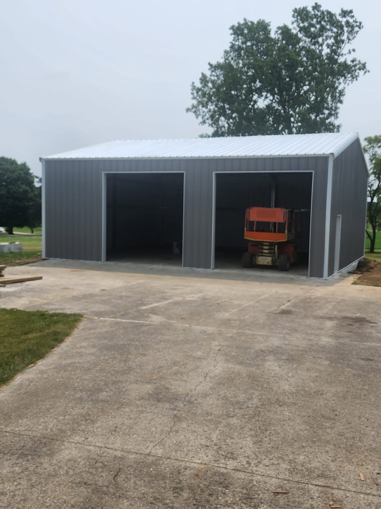Metal shed with two open bays; an orange tractor sits inside beside a concrete driveway.