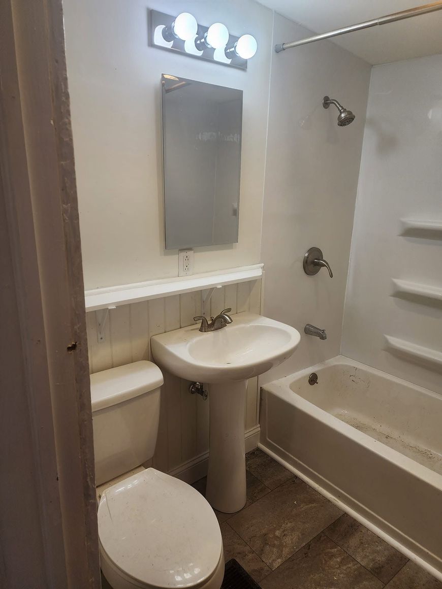 Small bathroom with toilet, pedestal sink, bathtub, mirror, and wall lights.