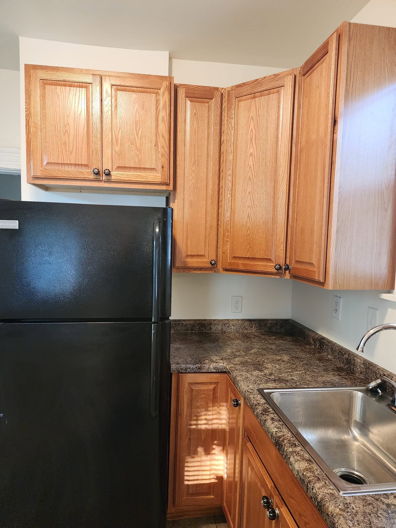Small kitchen with black refrigerator, wood cabinets, granite counter, and stainless steel sink