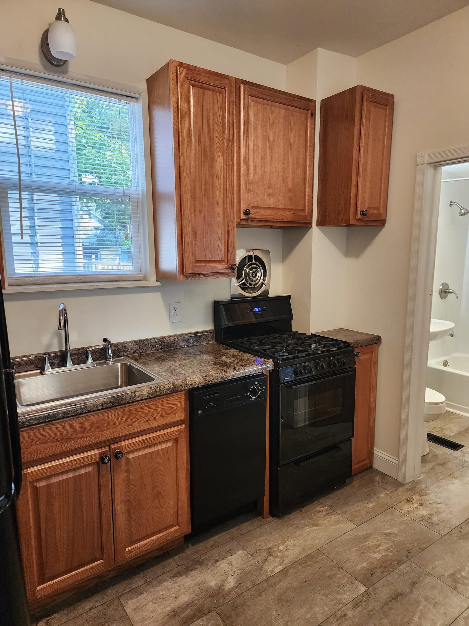 Small kitchen with wood cabinets, black appliances, granite countertop, sink by window, and tiled floor.