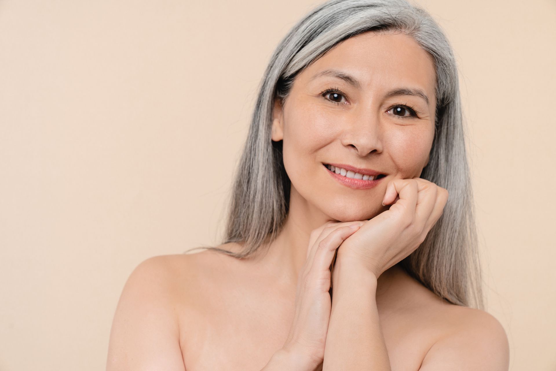 Una donna con i capelli grigi sorride e si tocca il viso con le mani.