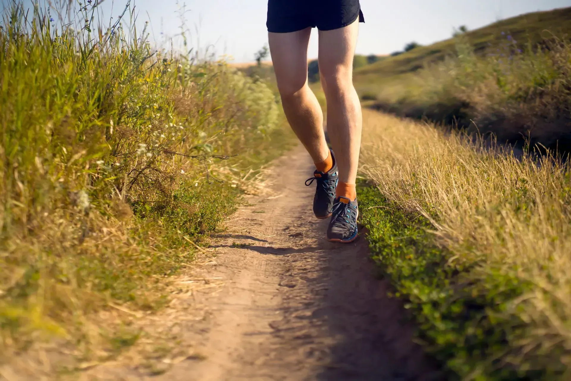 Runner jogging on a dirt trail through tall grass in warm sunlight