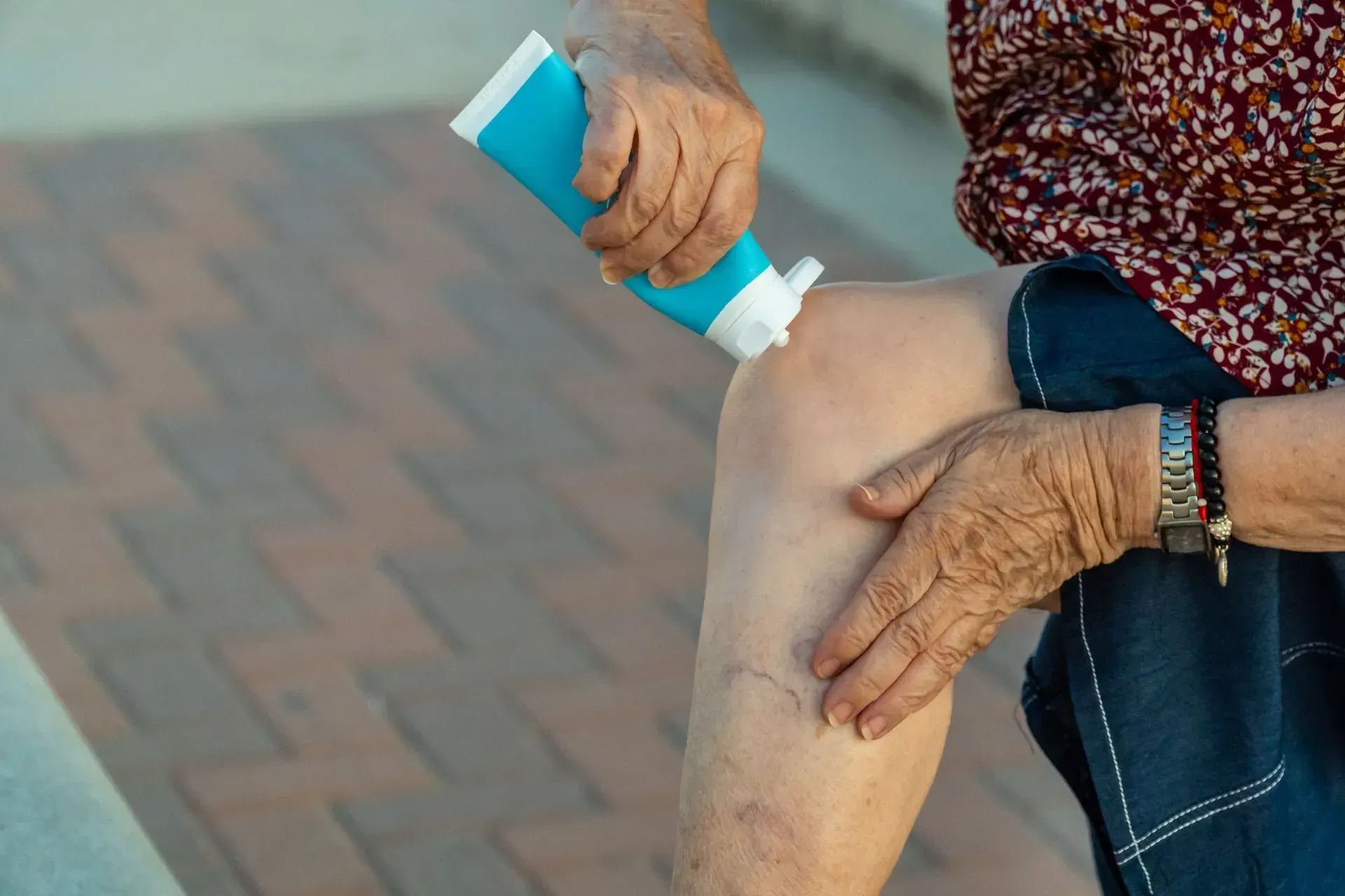 Applying sunscreen to a knee outdoors on a brick path