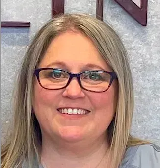 Smiling woman with blonde hair and glasses against a textured wall
