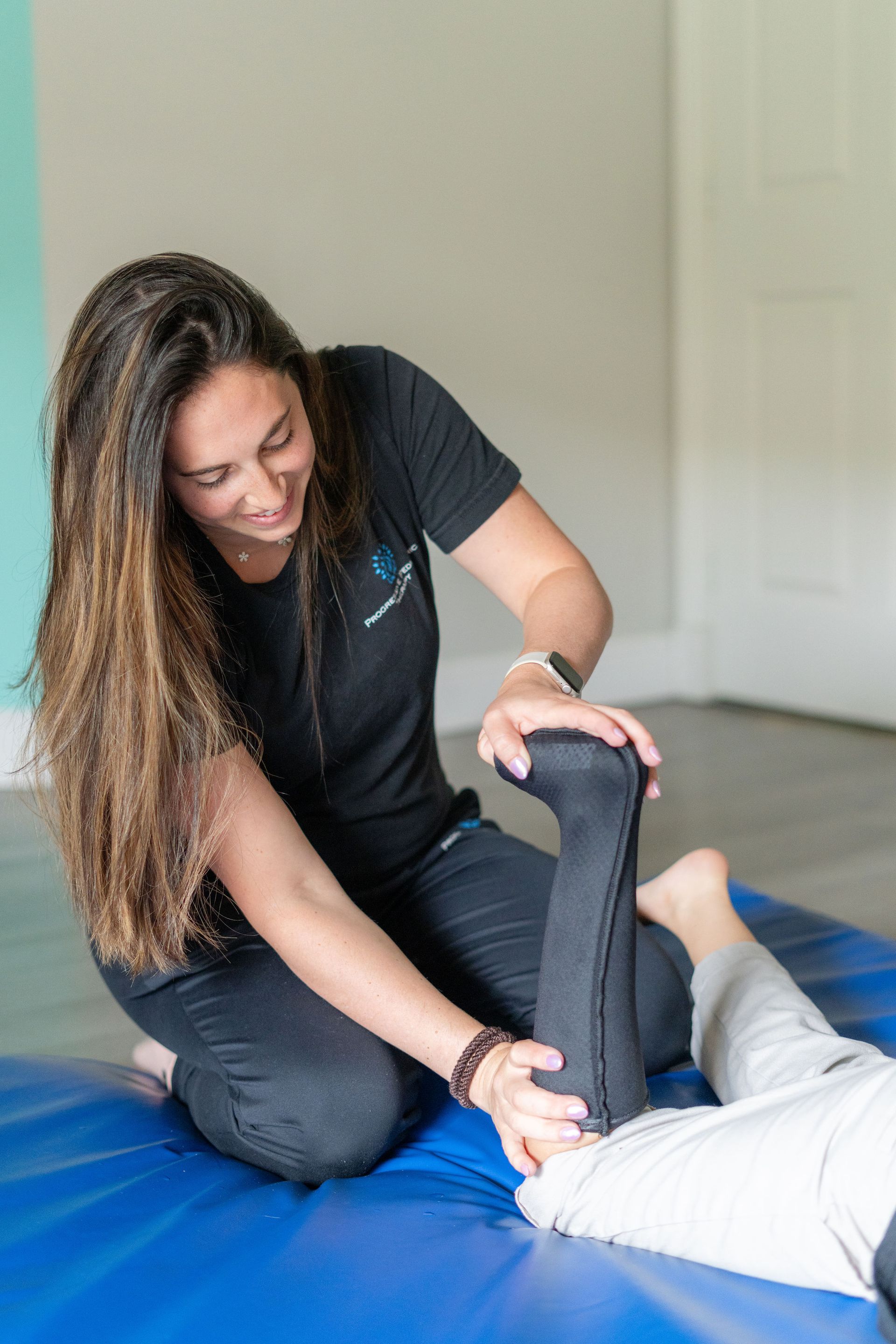 A woman is stretching a child 's leg on a blue mat.