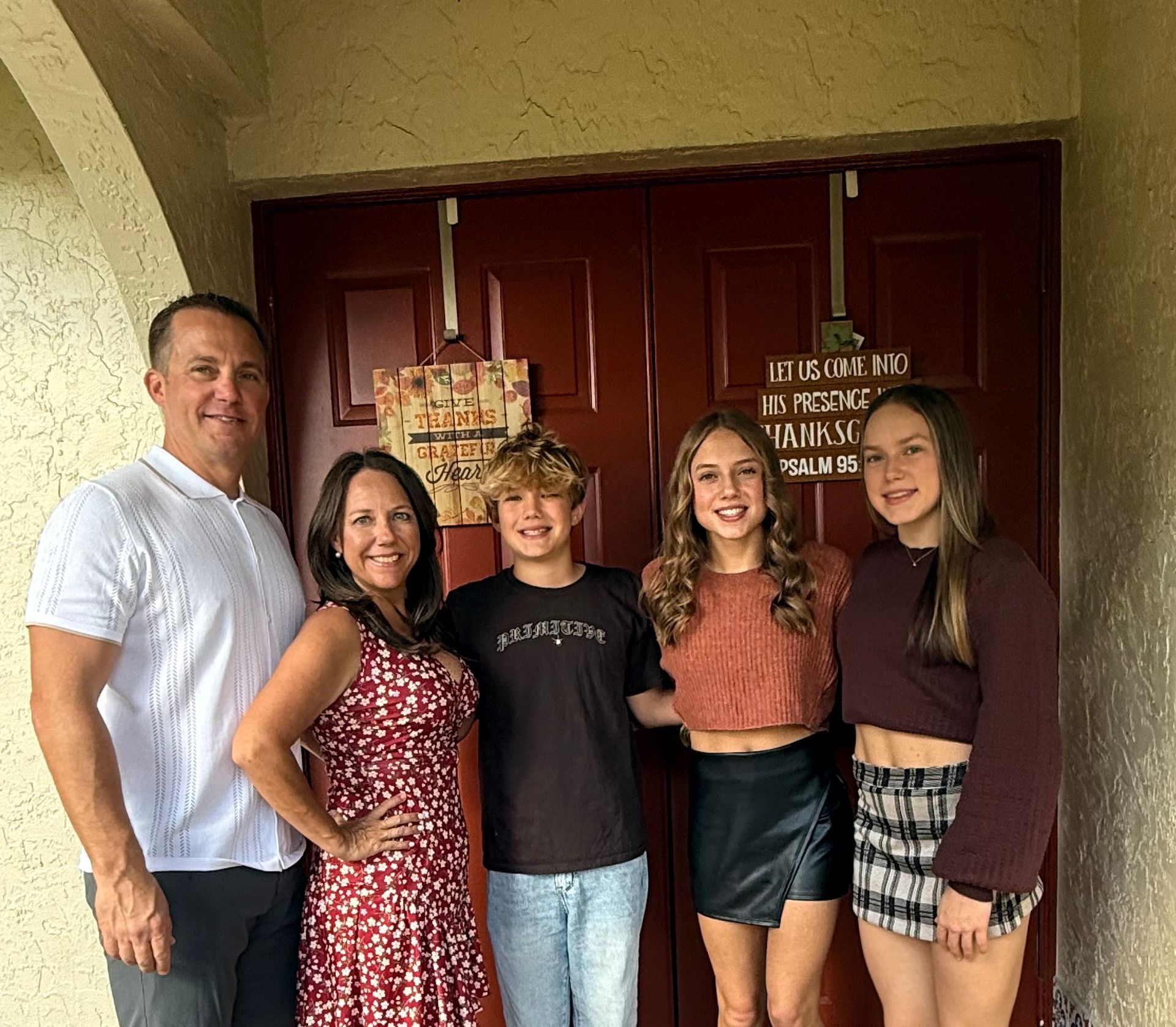 Family of five poses in front of a maroon door.