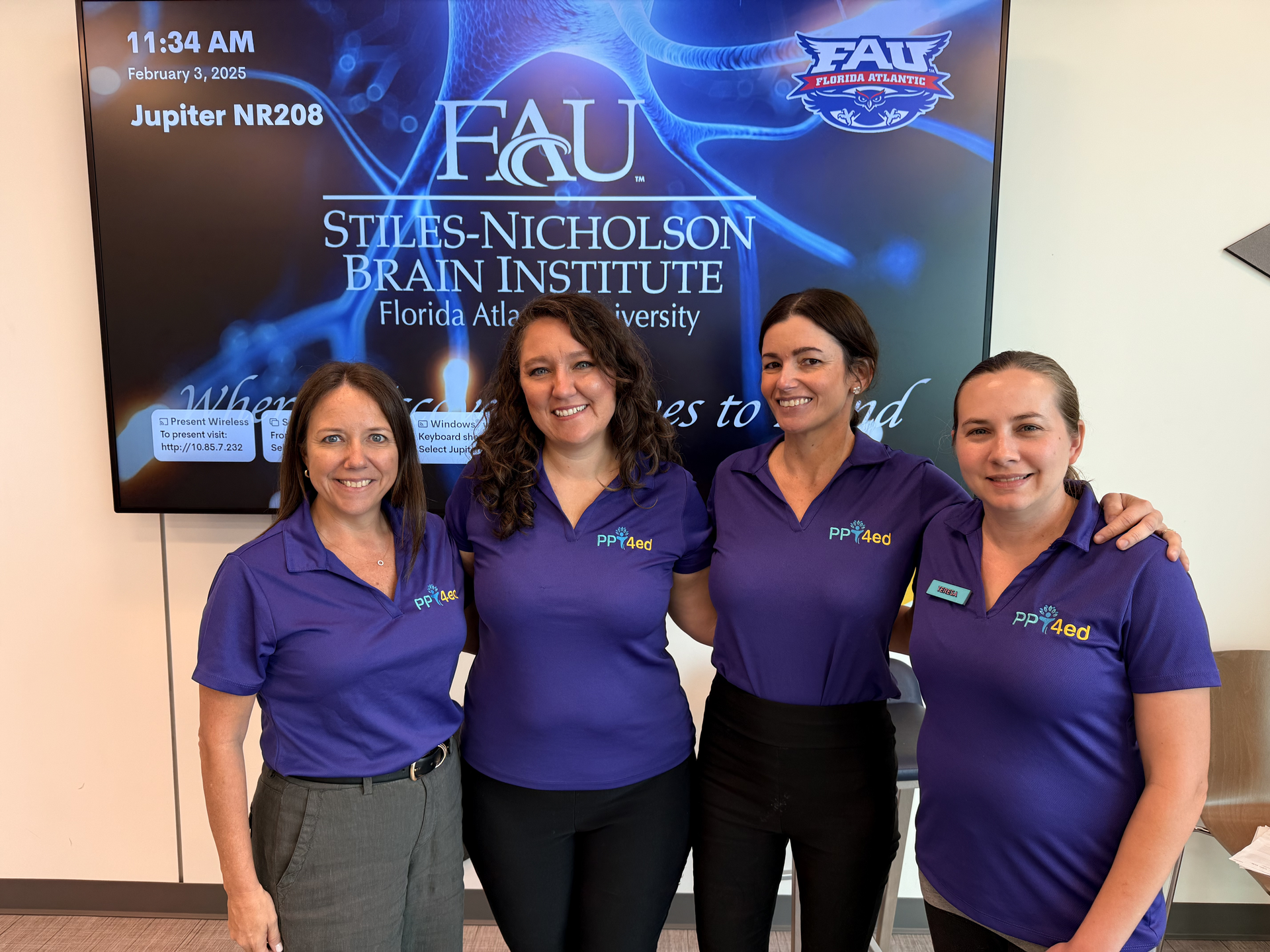 Four women in purple shirts pose in front of an FAU sign, likely at a brain institute.