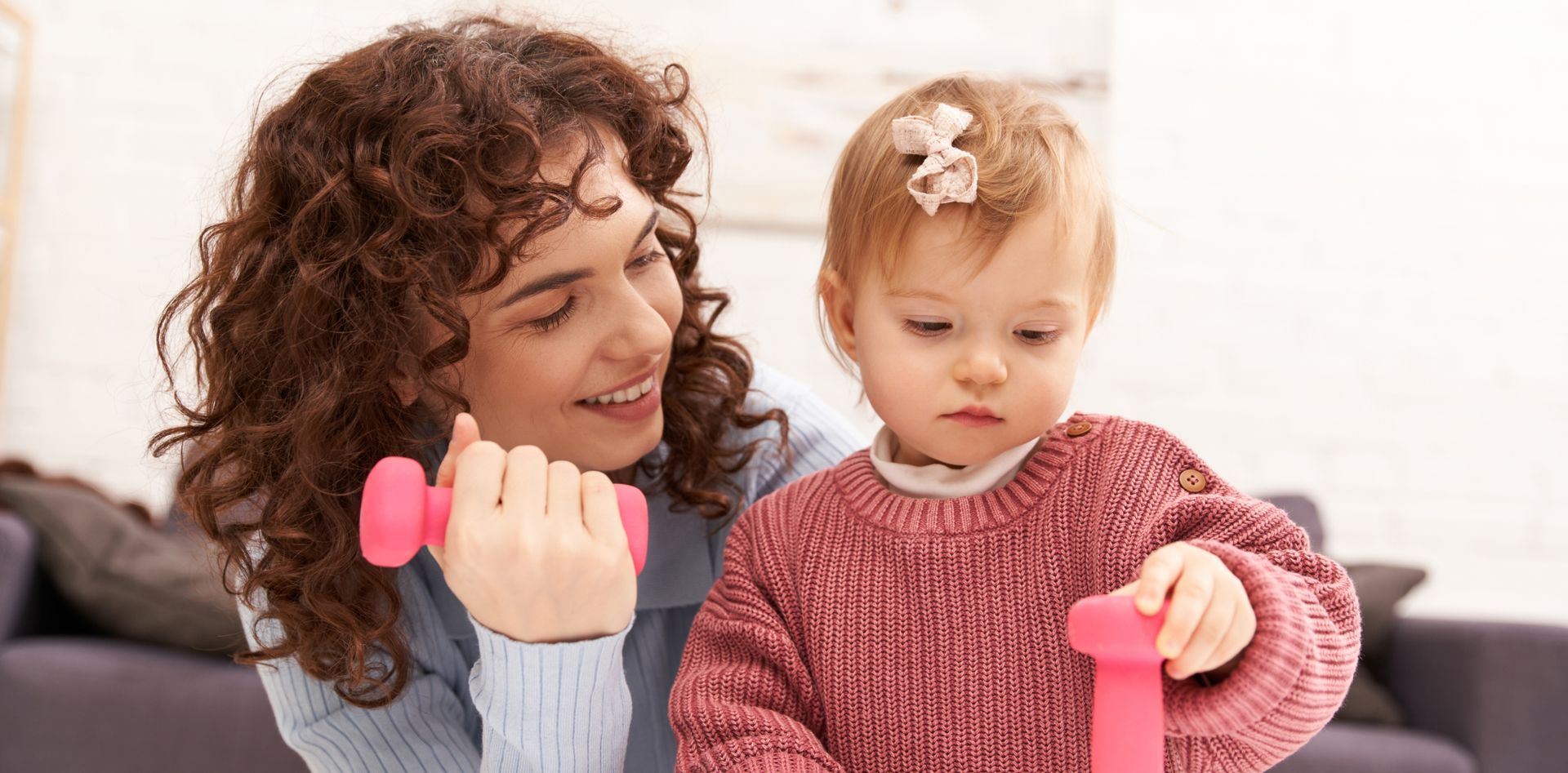 A woman is holding a pink dumbbell next to a baby girl.