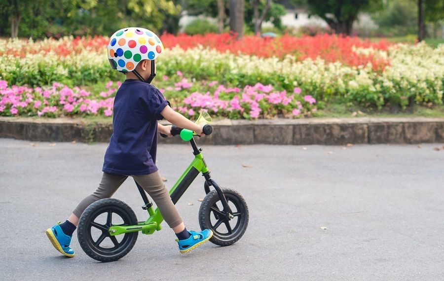 A young boy wearing a helmet is riding a balance bike.