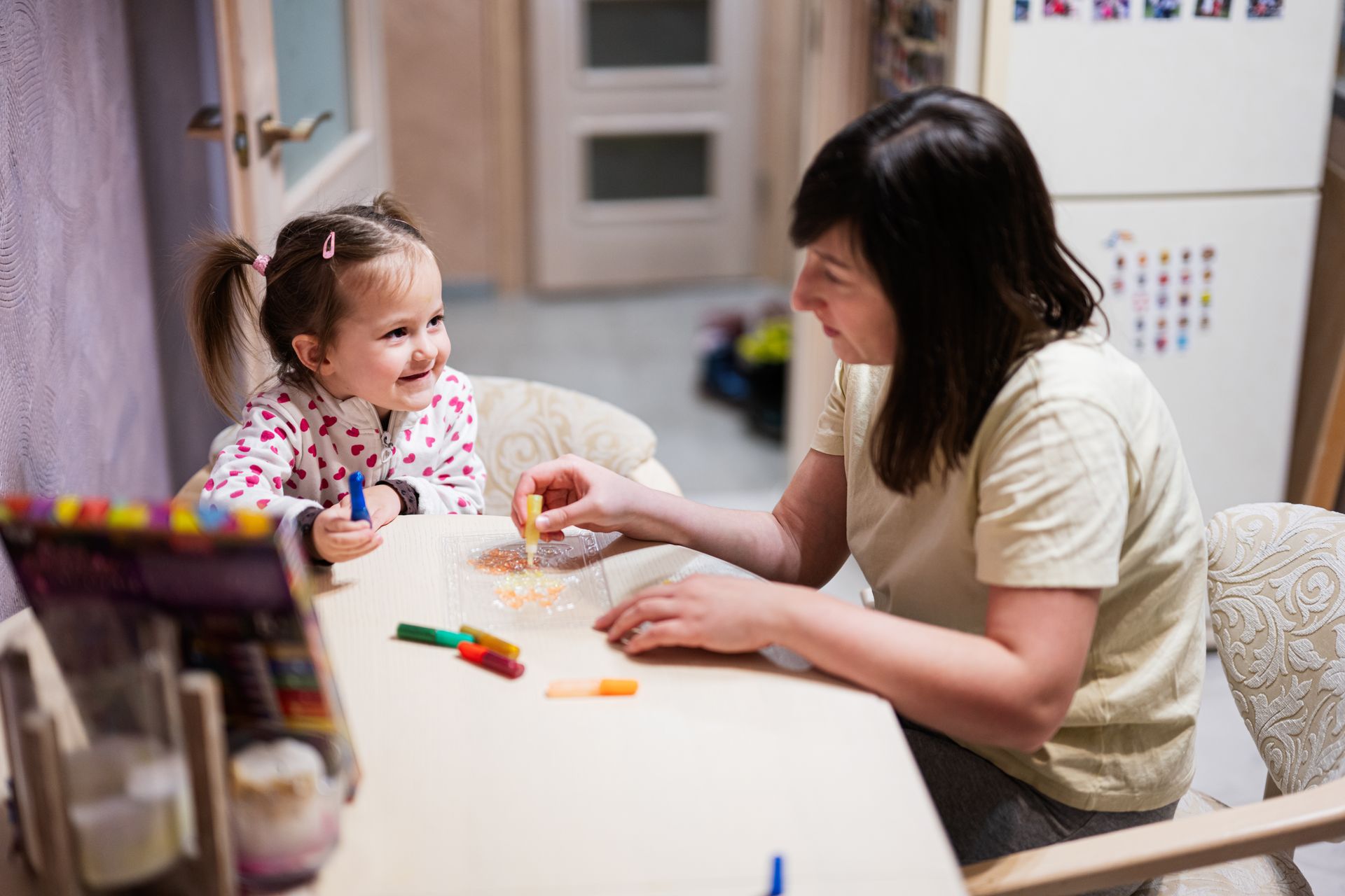 Woman and child painting at a table with colorful art supplies in a bright room