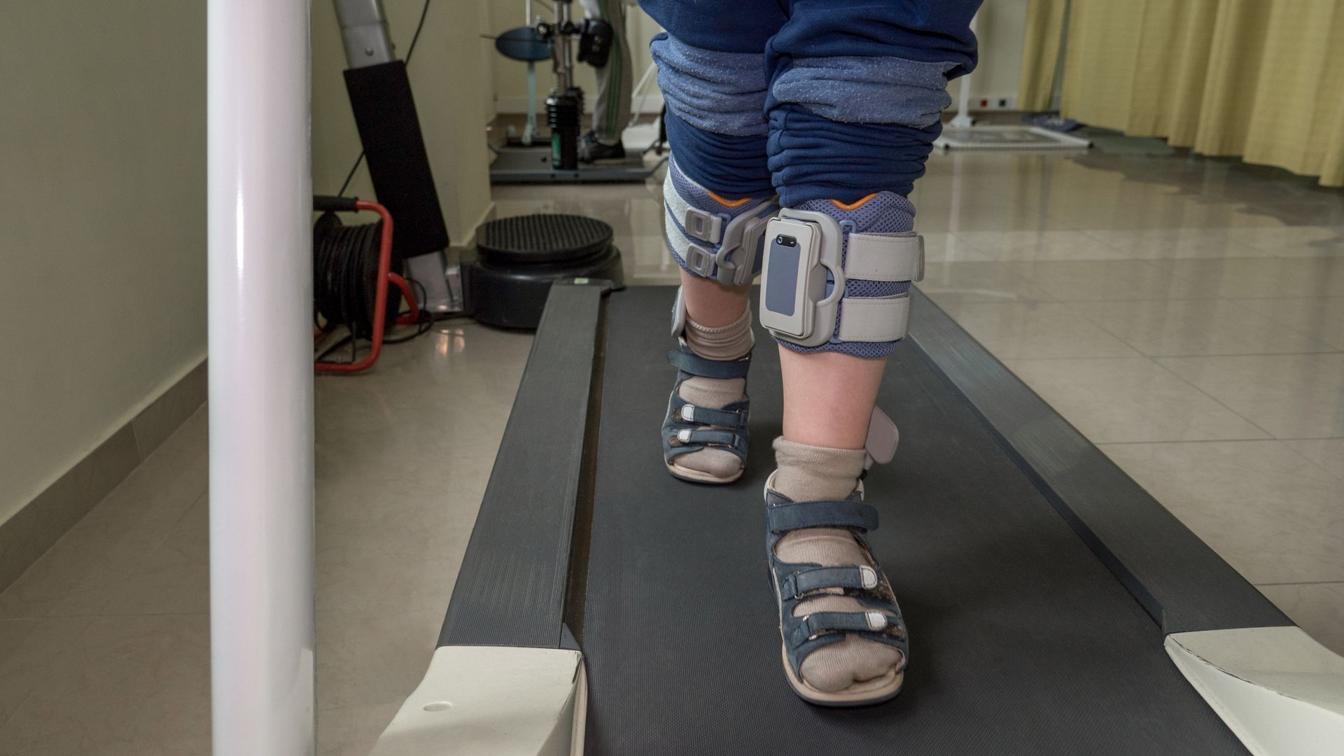 Child walking on a treadmill with leg braces and sandals in a clinic setting