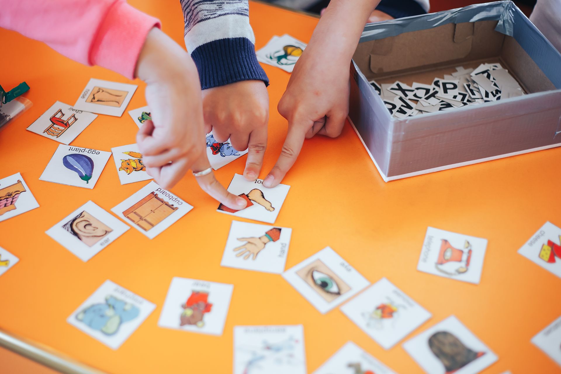 Hands sorting small picture cards on an orange table beside a gray tray