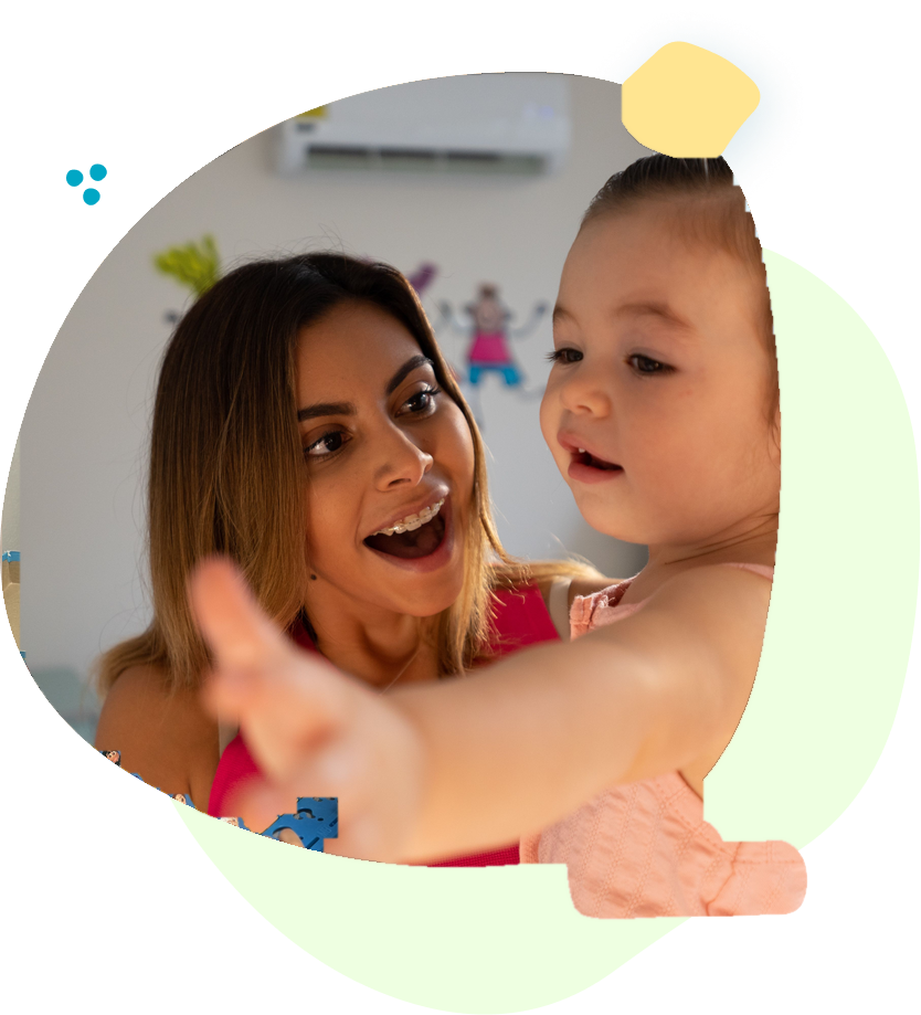 Smiling adult with baby indoors, reaching toward the camera in a bright, playful moment