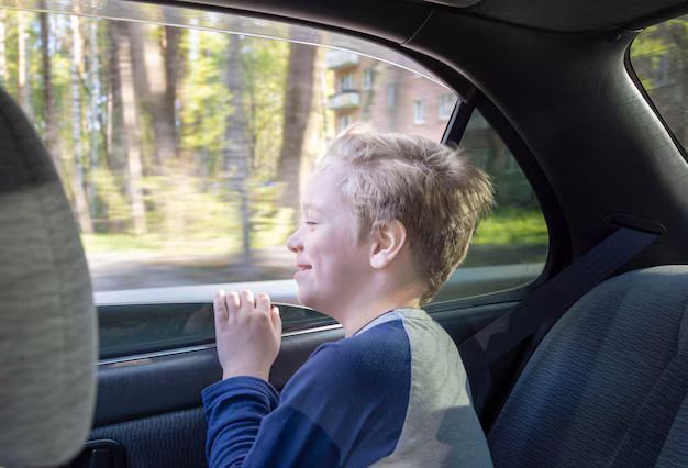 A young boy is sitting in the back seat of a car looking out the window.