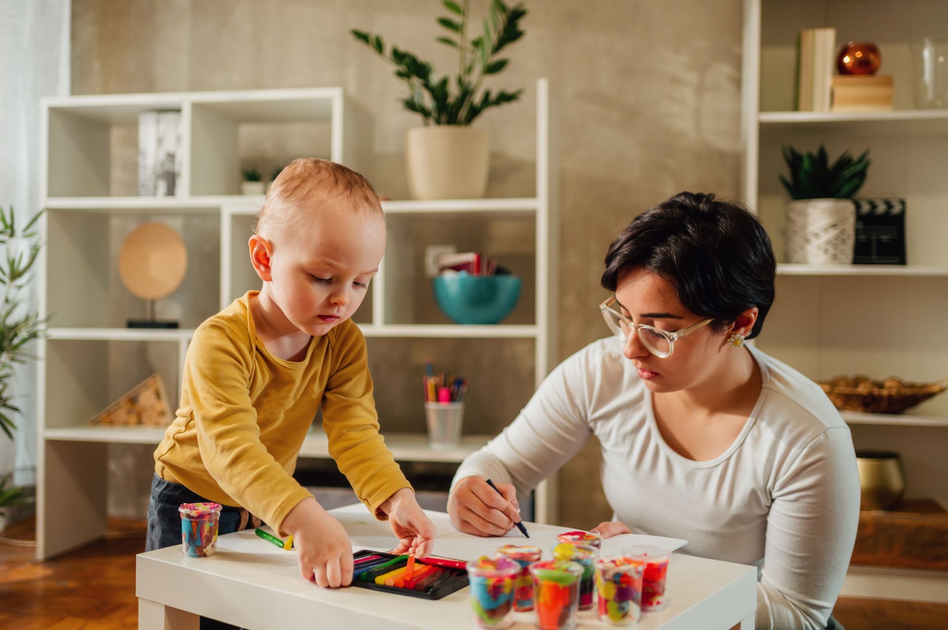 A woman and a child are sitting at a table playing with crayons.