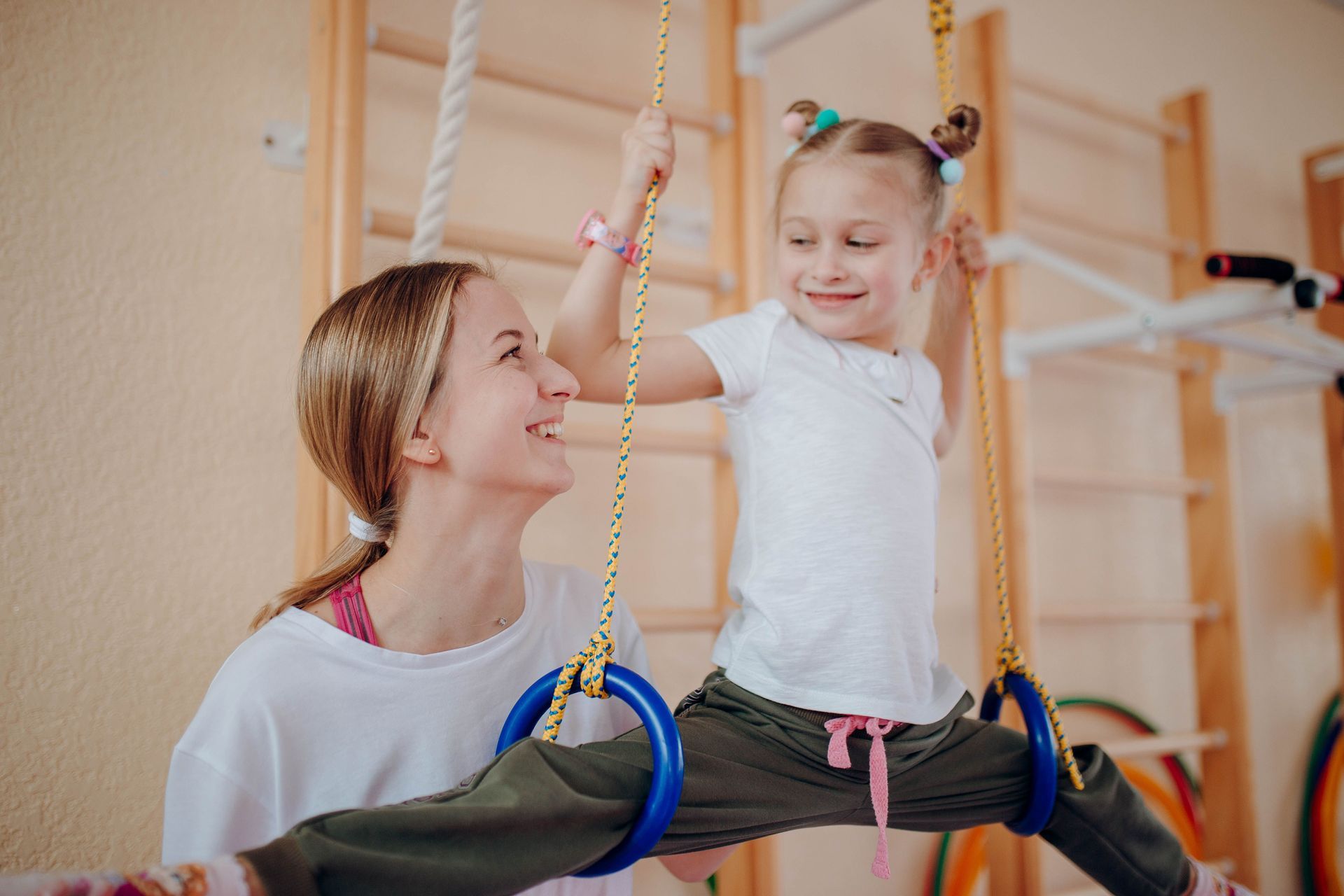 Woman and child on indoor swing, smiling and holding colorful beaded handles