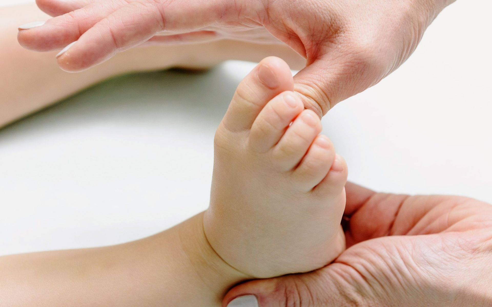 Adult hands gently holding a baby's foot against a white background