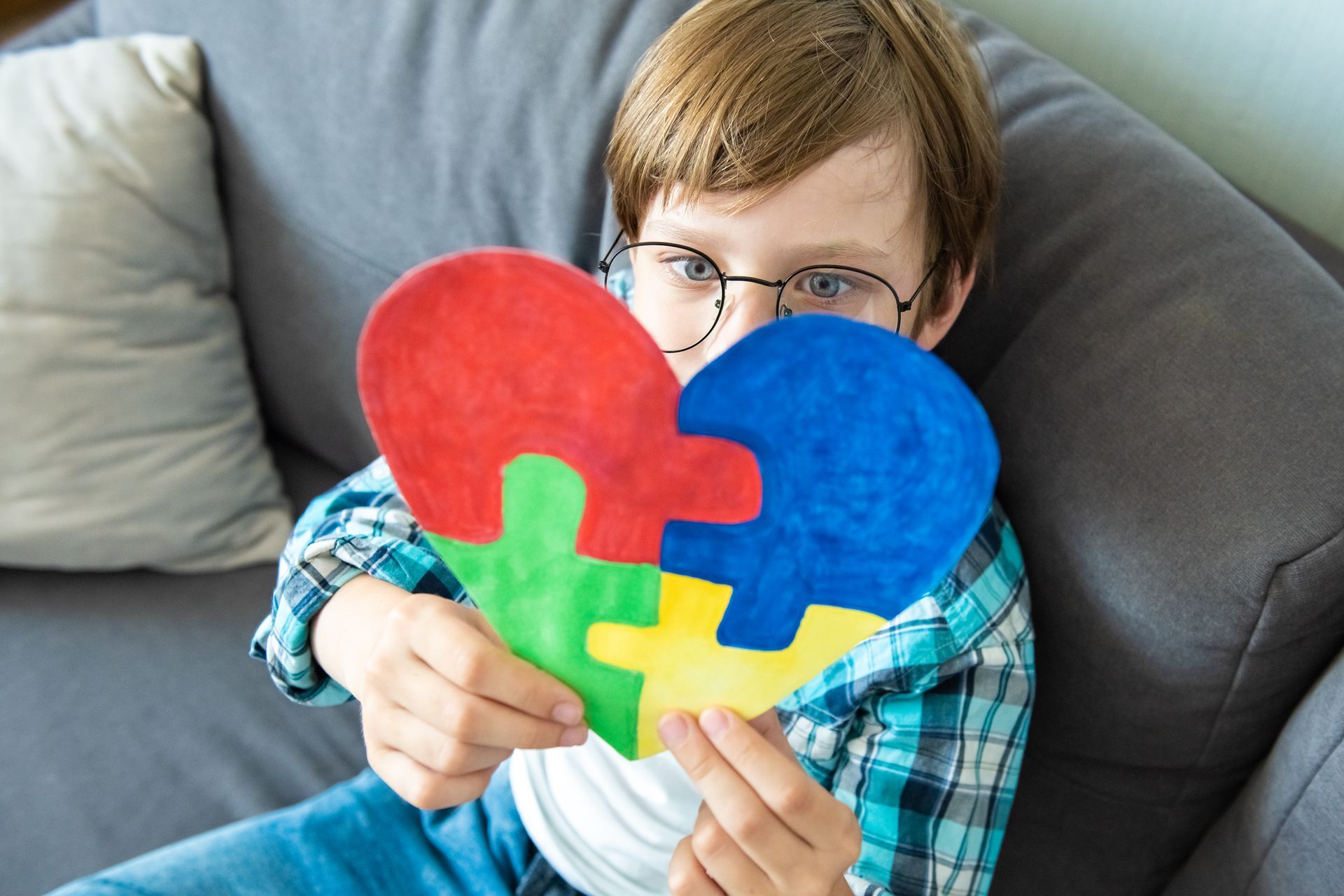 A young boy is sitting on a couch holding a heart made of puzzle pieces.