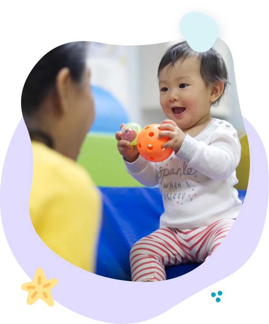 A baby is playing with an orange ball while a woman looks on.