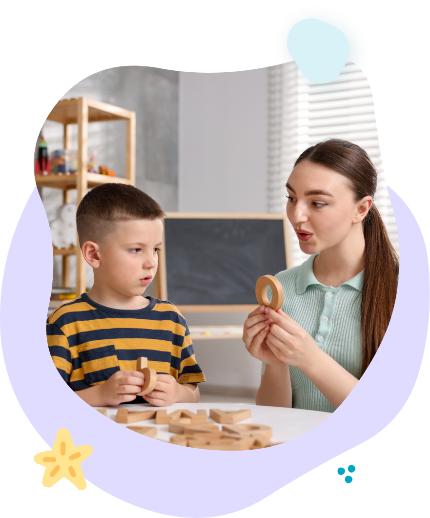 Teacher showing a wooden toy to a child at a table in a bright classroom