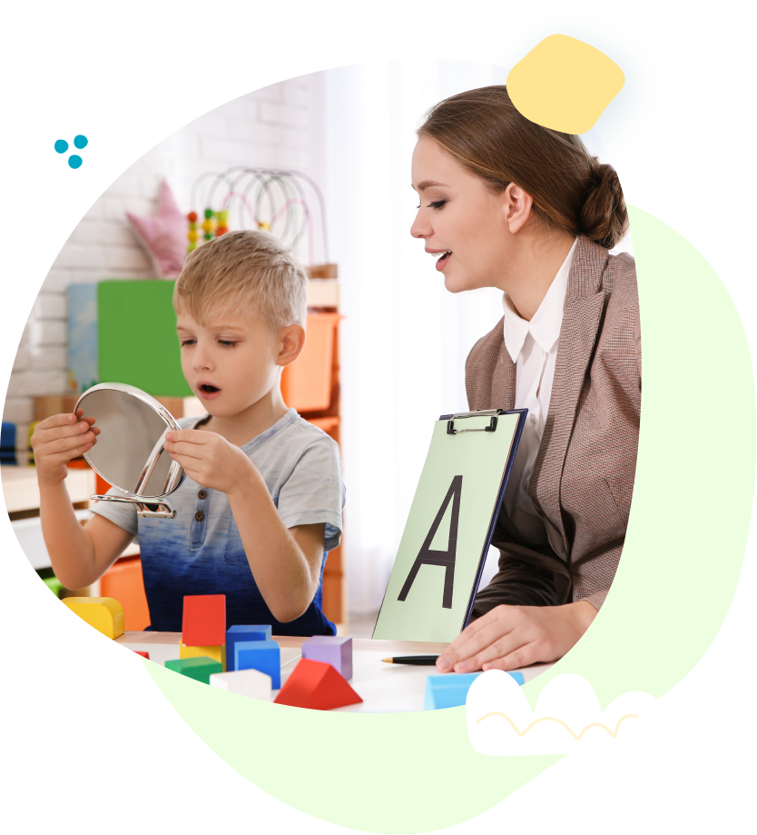 Teacher and child at a classroom table with colorful blocks, looking at a mirror and a letter card 