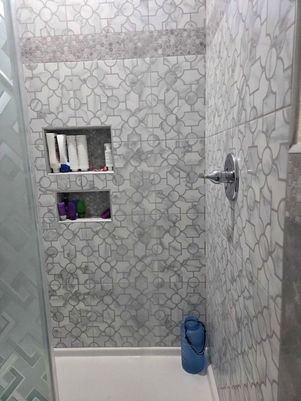 Small tiled bathroom with a shower/tub, recessed shelf, and blue bottle on the ledge.