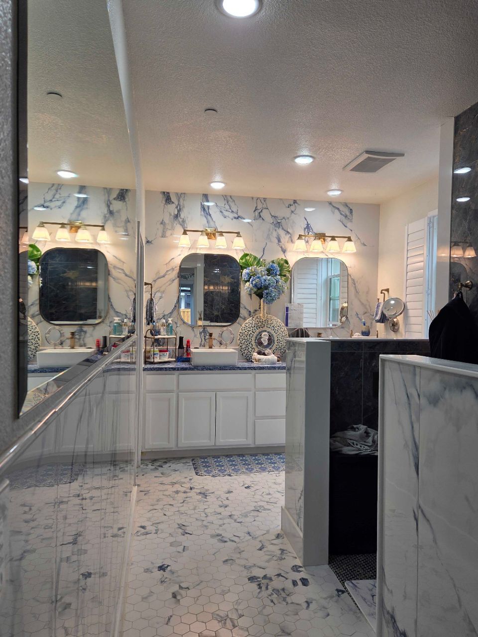 Modern bathroom with marble walls, double vanity, mirrors, and a person standing near the sink