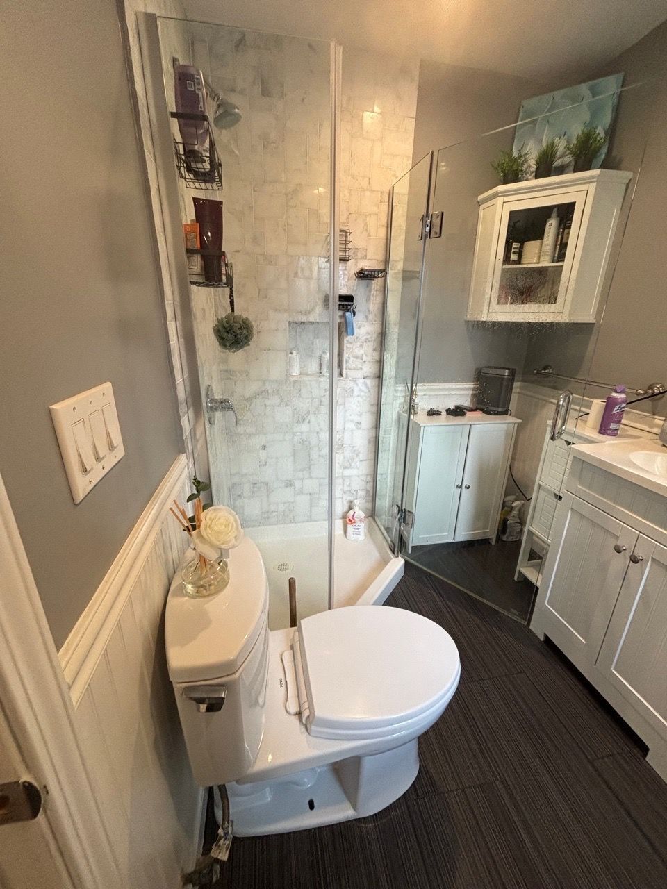 Small bathroom with a toilet, glass shower, white vanity, and gray walls and floor