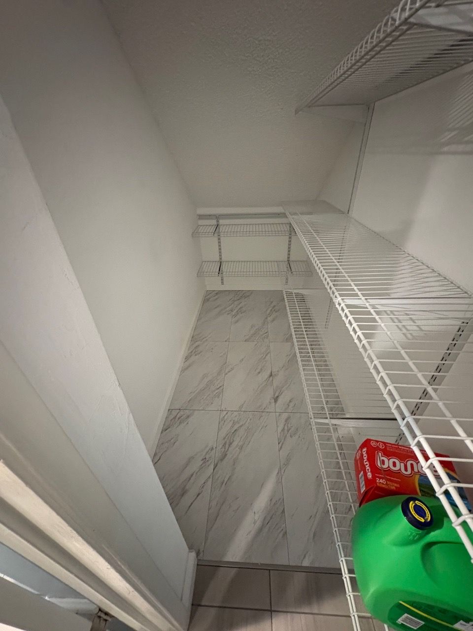 Empty white walk-in closet with wire shelving and a few items on the floor.
