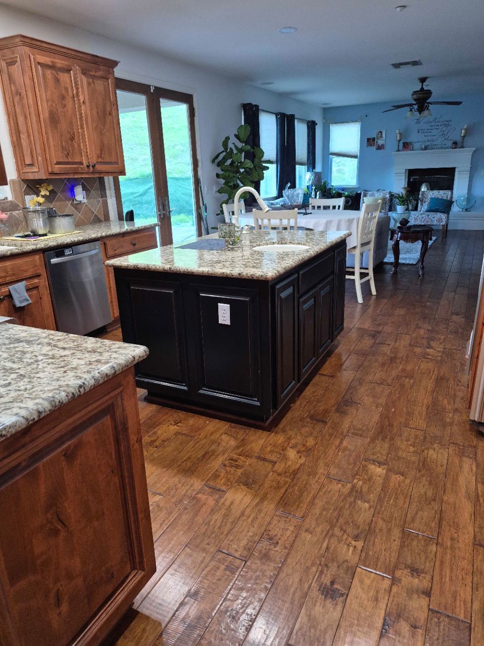 Bright kitchen with dark wood floors, island, and white dining area leading to a living room with fireplace.