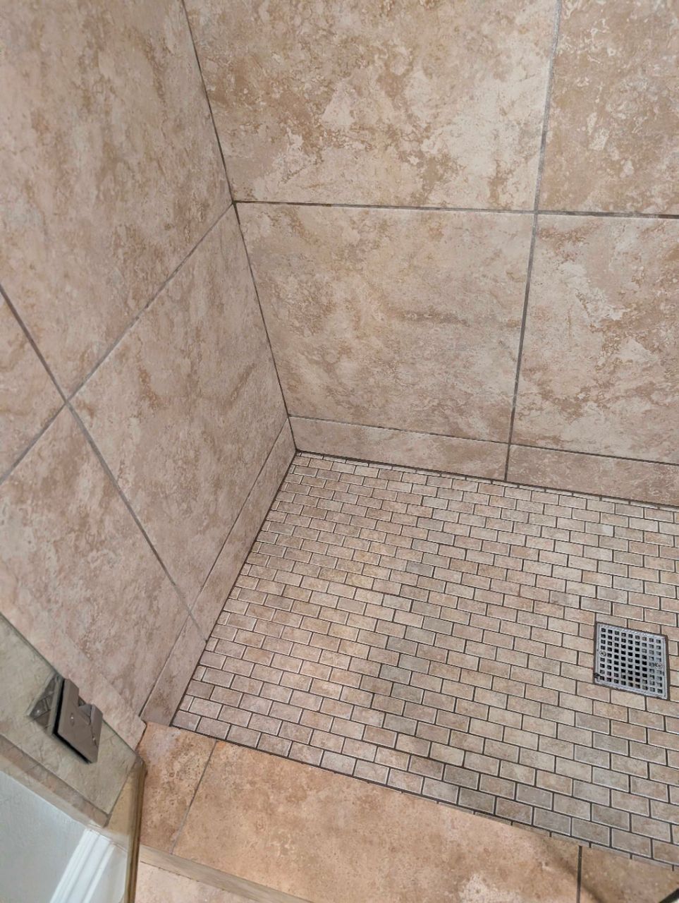 Tiled shower stall with beige walls, floor drain, and shower control handle.