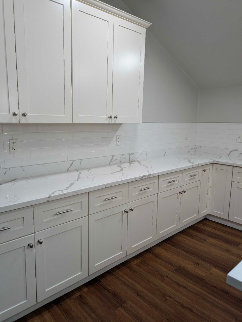 White kitchen with marble-look countertops, light cabinets, and wood flooring along a sloped wall