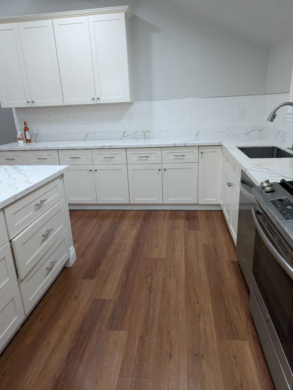 Modern white kitchen with wood-look flooring, white cabinets, and stainless steel stove and sink