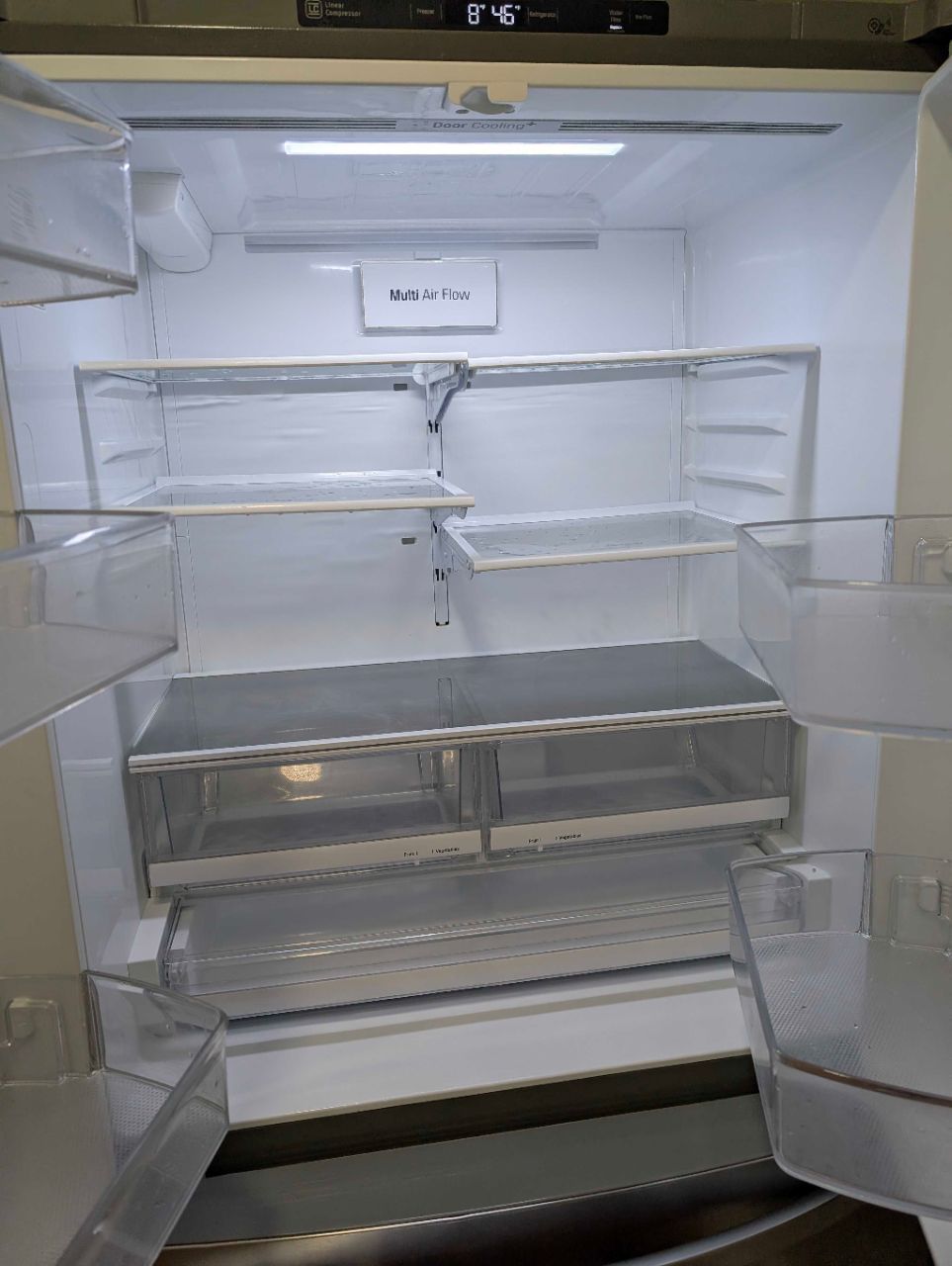 Empty open refrigerator with glass shelves and clear plastic drawers inside.