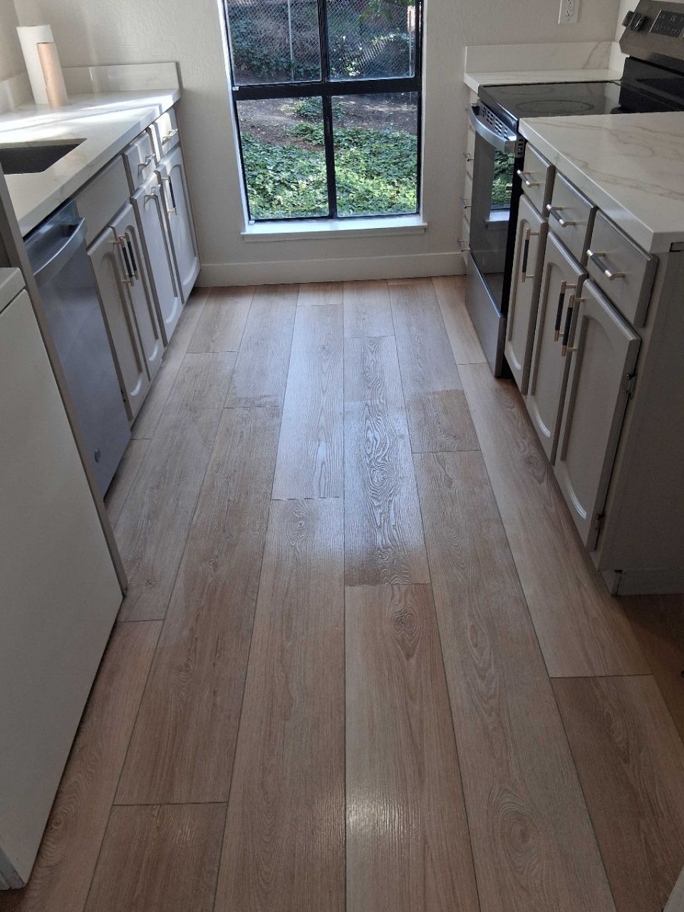 Narrow kitchen with light wood floor, gray cabinets, stainless appliances, and a glass door at the end.