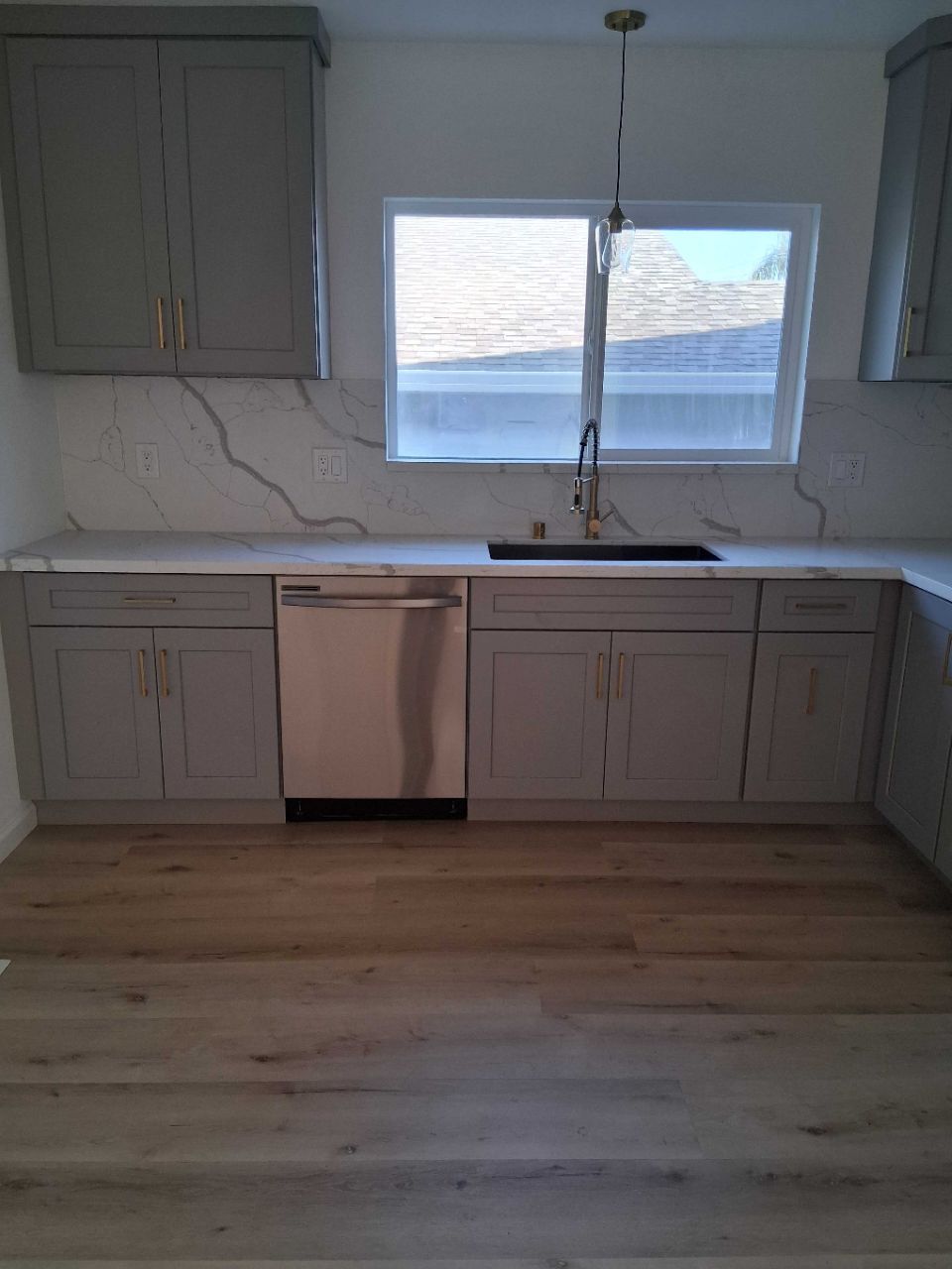 Empty modern kitchen with light cabinets, marble-look backsplash, stainless dishwasher, and window over sink.