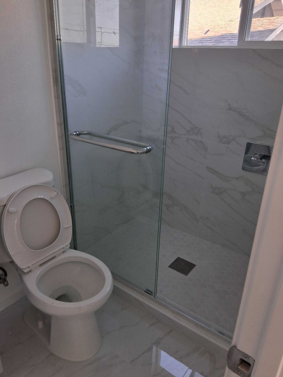 Small tiled bathroom with an open toilet and glass shower enclosure next to it.