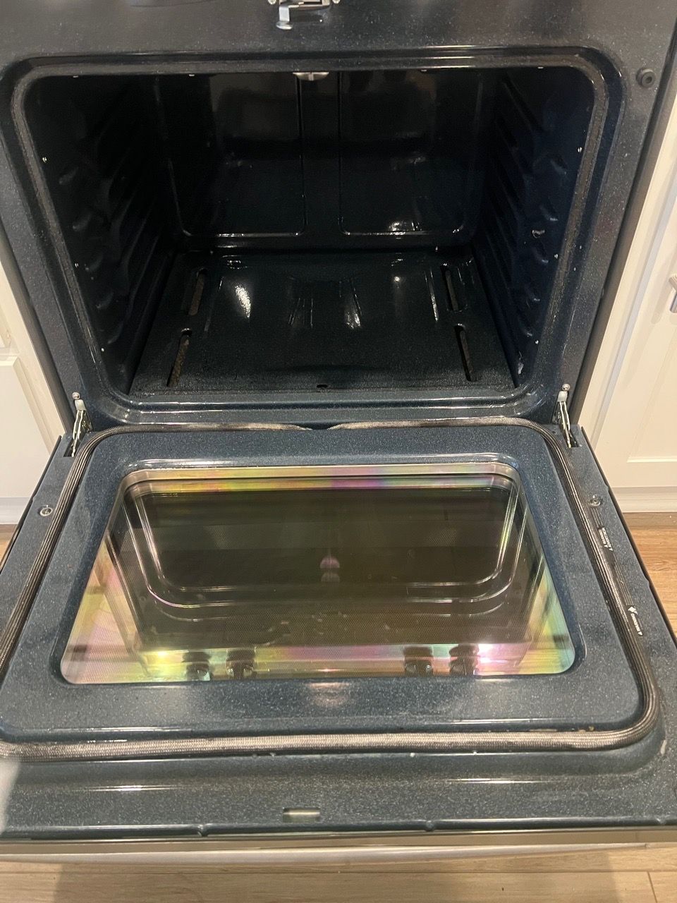 Open oven door with empty black interior and reflective glass panel on the front.