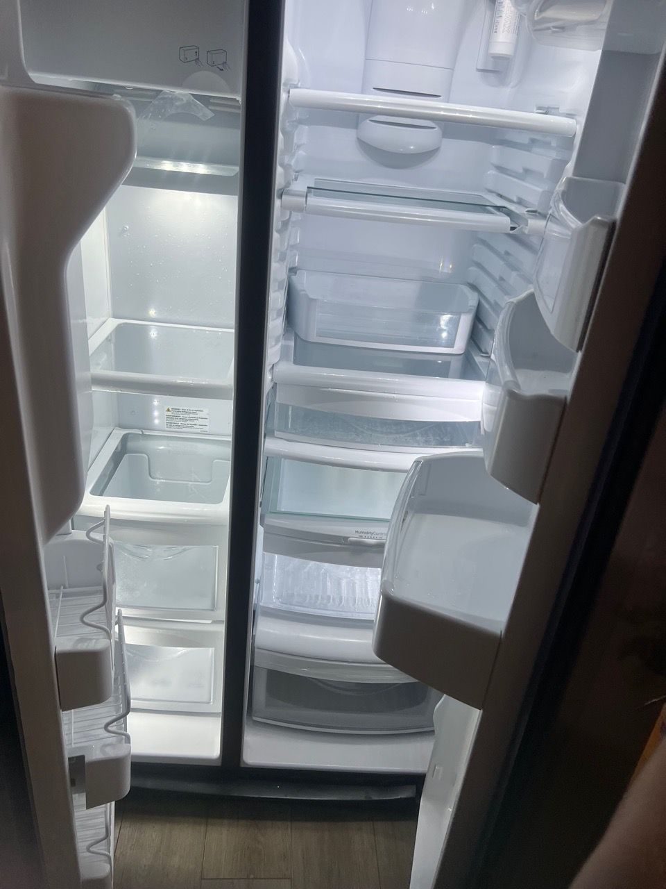 Open refrigerator with empty glass shelves and door bins, lit from inside.
