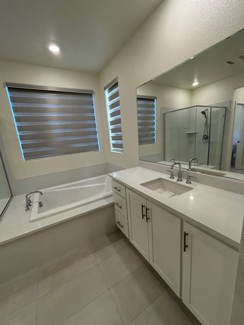Bright modern bathroom with double vanity, large mirror, tub, and tiled floor