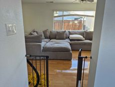 Living room with gray sectional sofa, wood floor, and large window overlooking a fenced yard