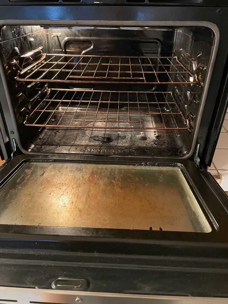 Open oven with wire racks and a dirty, grease-stained bottom tray
