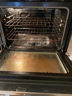 Open oven with wire racks and a dirty bottom tray inside