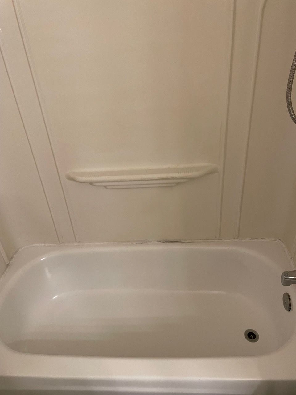 Bathtub with built-in grab bar and showerhead on the right side, viewed from inside the tub