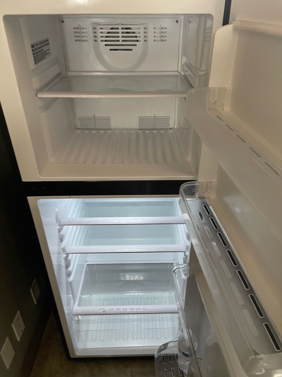 Open refrigerator with empty shelves and door compartments, interior light on.