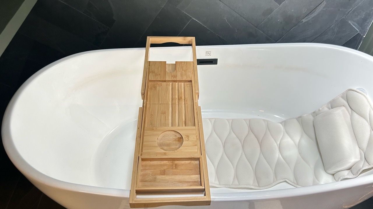White bathtub with a wooden bath tray and a white quilted bath pillow inside
