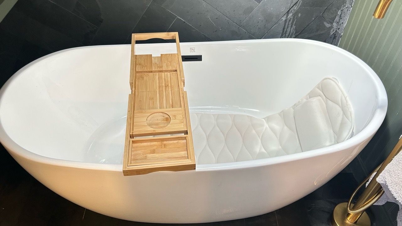 White oval bathtub with a wooden bath tray and quilted bath pillow in a tiled bathroom
