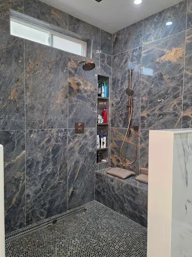 Gray marble walk-in shower with mosaic floor, recessed shelf, and small window near the ceiling