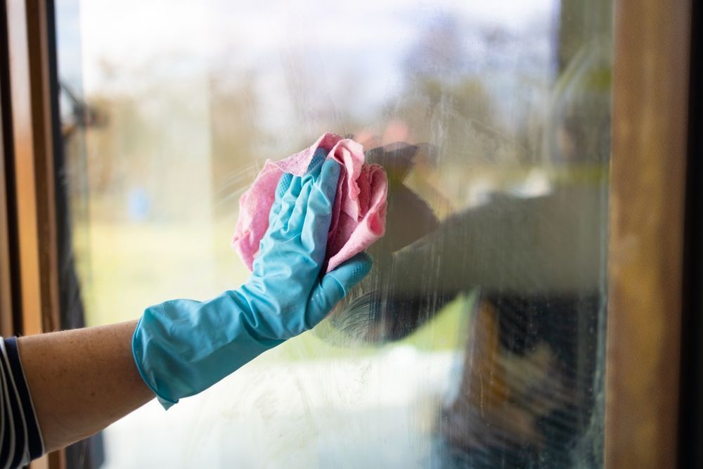 Gloved hand wiping a window with a pink and blue cloth