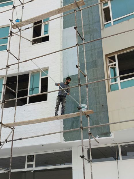 Worker on scaffolding painting the exterior of a white building.